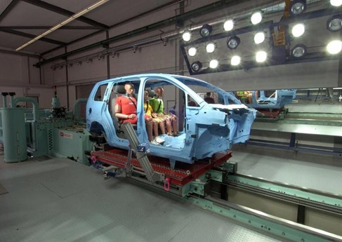 Tres maniquíes de pruebas de choque en el asiento trasero del chasis de un automóvil con las puertas y el conjunto frontal desmontados.